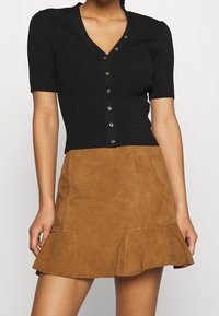 Black ribbed short-sleeve top with a V-neck and button closure paired with a brown suede flared mini skirt featuring side pockets.