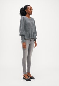 Grijze gebreide cardigan met ronde halslijn en knoopsluiting. Gecombineerd met slimfit grijze jeans en zwarte slingback schoenen met versieringen.