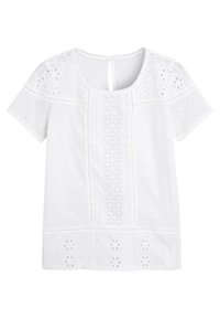 Blouse blanche à manches courtes avec broderie ajourée, présentant des motifs floraux, des panneaux texturés et un col rond avec fermeture par bouton à l'arrière.