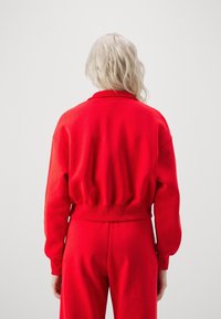 Röd sweatshirt med rundad krage, ribbade ärmslut och midja. Tyget verkar mjukt med en avslappnad passform, parat med matchande underdelar.