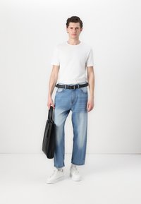 Camiseta blanca de manga corta, jeans sueltos de color azul claro, cinturón negro, llevando una bolsa tote negra y zapatillas blancas. Un atuendo simple y casual.