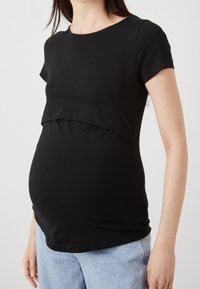 Zwart zwangerschaps-t-shirt van zachte katoen met een ronde halslijn, korte mouwen en een gelaagd voorpand, ontworpen voor een groeiende buik.