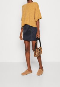 Khaki oversized stickad tröja, marinblå mini kjol, bruna pälsiga slip-on skor och en leopardmönstrad crossbody-väska med svart rem.