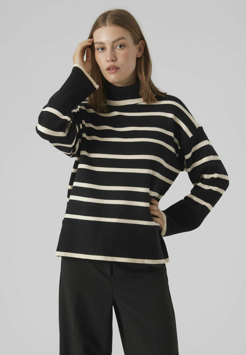 Un pull rayé noir et crème avec un col montant, des poignets côtes et une coupe décontractée, associé à un pantalon noir. Texture en maille douce.