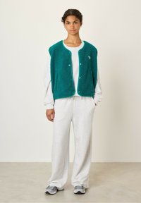 Teal fleece vest met ronde halslijn, drukknopen en zijzakken, gedragen over een grijze sweatshirt en bijpassende sweatpants.