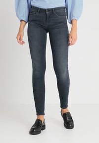 Jeans ajustados de color azul oscuro hechos de denim, con un diseño estándar de cinco bolsillos, pasadores para cinturón y un acabado suave. Combinados con mocasines negros.
