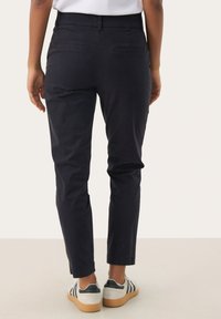Chinos blu navy con una vestibilità affusolata, dotati di una vita piatta e due tasche posteriori. Indossati con sneakers grigie e strisce bianche.