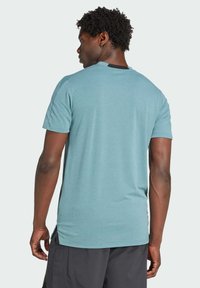 T-shirt bleu clair à manches courtes en tissu doux, avec un col rond et une coupe décontractée. Le dos a une texture lisse sans graphismes.