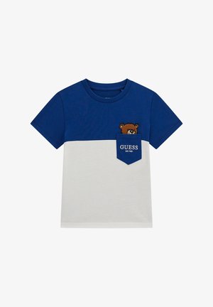 Sinine ja valge puuvillane T-särk lühikeste varrukatega, mille rinnataskul on karu tikand ja tekst "GUESS EST.1981."