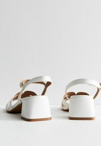 Sandali bianchi con tacco a blocco e cinturini alla caviglia, con finitura opaca e interno color nocciola, mostrano un design aperto della punta e del retro.