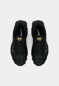 Černé tréninkové boty Nike s texturovaným svrškem, zlatými akcenty a šedými detaily loga. Mají šněrovací design a polstrovanou podrážku.