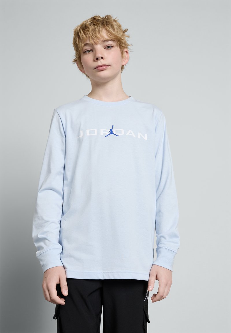 Lyseblå langermet skjorte med "JORDAN" trykket i hvitt og en blå Jumpman-logo. Har rund hals og en avslappet passform.