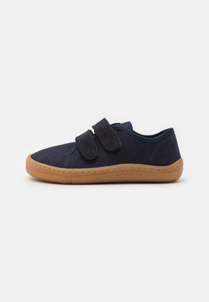 Zapatilla deportiva de tela azul oscuro con suela marrón y dos tiras de velcro ajustables, mostrada de lado sobre un fondo blanco.