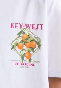 Witte katoenen t-shirt met een kleurrafisch ontwerp van sinaasappels met groene bladeren, "KEY-WEST" tekst hierboven en "PETROL IND" eronder in het roze.