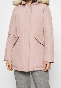 Light pink padded parka with a faux fur hood, front zip, and side pockets. Smooth fabric with a relaxed fit and mid-length design.