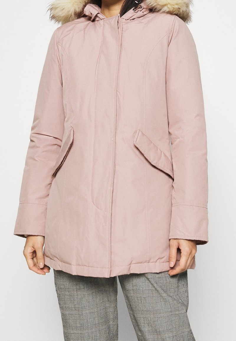 Light pink padded parka with a faux fur hood, front zip, and side pockets. Smooth fabric with a relaxed fit and mid-length design.