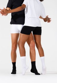 Zwart-witte boxershorts gecombineerd met bijpassende crew-sokken. Zwart t-shirt contrasteert met witte shirt, beide hebben een losse pasvorm en korte mouwen.