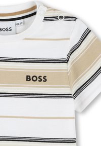 T-shirt in cotone con righe orizzontali beige, bianche e nere, con scollatura rotonda e bottoni a pressione sulla spalla. Logo "BOSS" stampato.