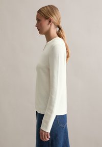 Hellbeige langärmliges Oberteil mit gerippter Textur, runder Ausschnitt und lässiger Passform, kombiniert mit einem dunklen Jeansrock mit einer Gesäßtasche.