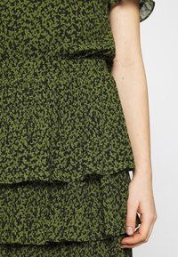 Top de tela con estampado floral verde, con volantes en varias capas; textura plisada; mangas cortas; la base negra resalta el diseño verde.