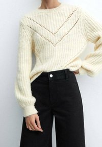 Pull tricoté crème avec un motif en chevrons, détails côtelés et manches longues, associé à un jean noir taille haute à jambes larges.