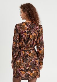 Robe à motifs floraux en tissu sombre, avec des manches longues, une taille cintrée avec une ceinture, et une courte encolure. Les couleurs incluent le violet, l'orange et le vert.