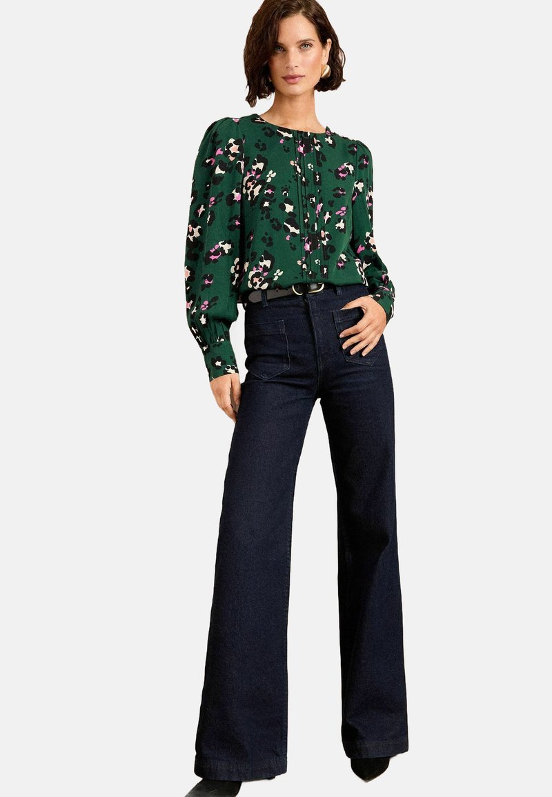 Groene bloemenblouse met pofmouwen, gecombineerd met donkerblauwe wijdbenige jeans. Blouse heeft knopen en een ontspannen pasvorm.