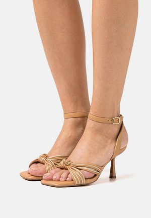 Beige hoge hakken sandalen met geknoopte voorkantontwerp, enkelbandje en textuurmateriaal. Heeft een smalle hak en open teen.
