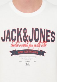 Λευκό βαμβακερό T-shirt με έντονο μαύρο και κόκκινο κείμενο, που περιλαμβάνει τις φράσεις "JACK & JONES" και "NEW AESTHETICS", με ομαλή υφή.