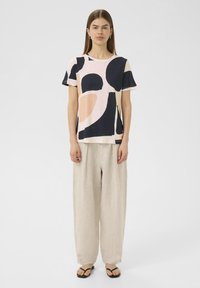 Tricou cu mânecă scurtă, cu un model abstract roz și bleumarin, dintr-un material ușor, cu o croială lejeră; asortat cu pantaloni lejeri din in bej și sandale negre.