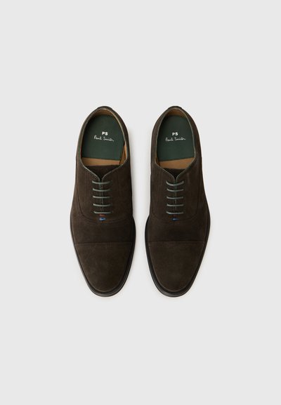 Scarpe in suede marrone con punta rotonda, cinque fori per i lacci, lacci verdi e suola in gomma nera. L'interno presenta una fodera verde con logo.