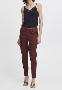 Camisole noire avec dentelle, associée à un pantalon taillé bordeaux et une ceinture marron. La tenue présente une coupe slim et des sandales à talons.