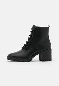Bottes de cheville noires à lacets en matériau synthétique, avec talon bloc, semelle texturée et languette à l'arrière.