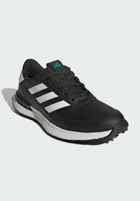 Svart atletisk sko med syntetisk overdel, sølvfargede detaljer, tre hvite striper, snøringsdesign og teksturert såle for grep.