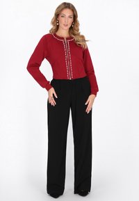 Sudadera roja recortada con detalles de botones, combinada con pantalones negros de pierna ancha. Tela lisa, ajuste estructurado y mangas largas.