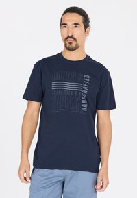 T-paita tummansinistä puuvillasta, jossa on lyhyet hihat, ja siinä on graafinen printti, jossa on vaaleampia sävyjä tekstillä ja viivoilla, sekä pyöreä kaula-aukko.