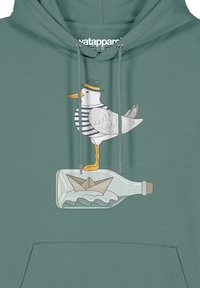 Türkise Kapuzenjacke mit einem Grafikdesign eines Möwe in einem Hut, die auf einer Flasche steht, neben einem Papierboot. Das Design umfasst gedämpfte Farben und verspielte Details.