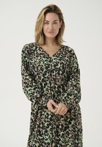 Ilga, žalia ir juoda leopardų rašto suknelė su V formos iškirpte, susirinkusia juosmens vieta ir ilgomis rankovėmis. Lengva medžiaga, laisvai krentanti.