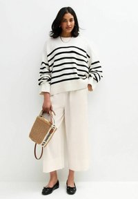 Crème en zwarte gestreepte trui, witte brede broek, zwarte flats en een geweven tas met een logo-riem. Zachte textuur, losse pasvorm.