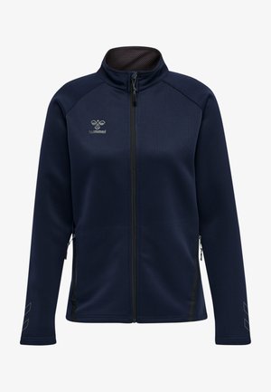 Granatowa bluza zapinana na zamek wykonana z miękkiego materiału, z bocznymi kieszeniami, wysokim kołnierzem i kontrastującymi zamkami błyskawicznymi. Na lewej piersi znajduje się logo.