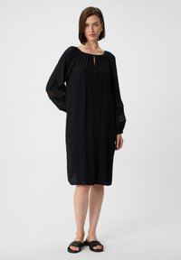 Zwarte jurk met lange, volumineuze mouwen met geborduurde details. Sleutelgat halslijn, knielengte, gemaakt van een lichtgewicht stof.