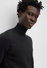 Pull à col roulé noir en tissu maille lisse. Présente un design ajusté avec une silhouette élancée et une texture subtile.