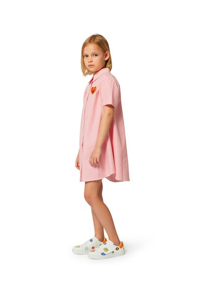 Robe chemise rayée rouge et blanche avec un col, ornée d'un patch en forme de cœur. Associée à des baskets blanches décorées de stickers colorés.