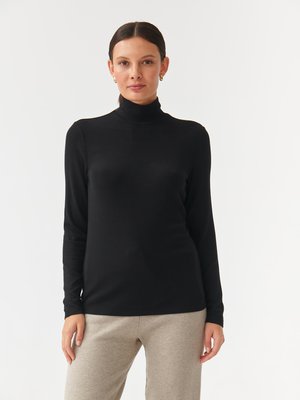 Black ribbed turtleneck top with long sleeves, featuring a fitted design. Paired with light grey, relaxed-fit pants.