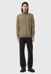 Olijfgroen, lange mouwen kwart-zip sweater met geribbelde manchetten en zoom, gecombineerd met zwarte rechte jeans en donkere schoenen.