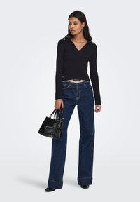 Pull noir en maille côtelée avec col en V et col contrastant, associé à un jean évasé foncé et un sac à main noir en simili-crocodile.