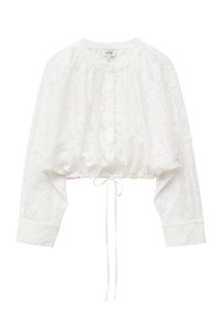 Blouse courte blanche à manches longues avec motifs floraux découpés, encolure ronde, boutonnée devant, ourlet élastiqué avec cordon noué.