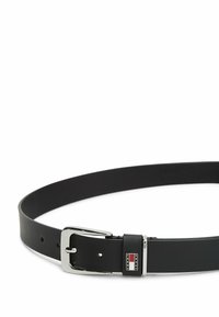 Cinturón de cuero negro con una hebilla metálica plateada, que presenta un acento de logo y orificios para ajuste, textura suave y sección transversal circular.