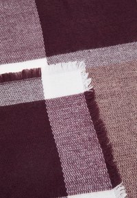 Écharpe à carreaux en marron et brun clair, fabriquée en textile doux avec des bords à franges. Présente des motifs alternés en finitions lisses et texturées.