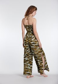 Jumpsuit brez naramnic v zeleni in beli tie-dye vzorcu; vsebuje smockan bodice, stranske odprtine in halter vrat z detajlom z resicami.